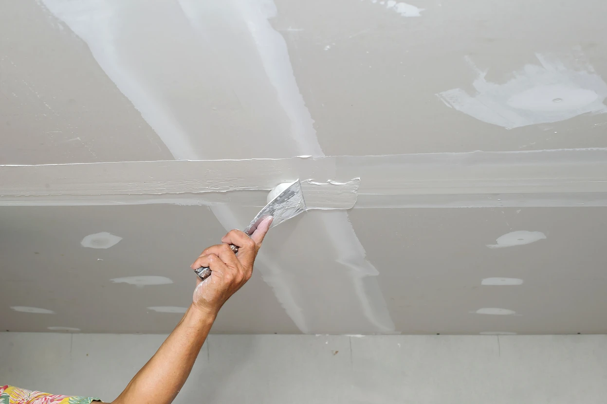 Intérieur résidentiel avec ouvrier effectuant des travaux de finition au plafond