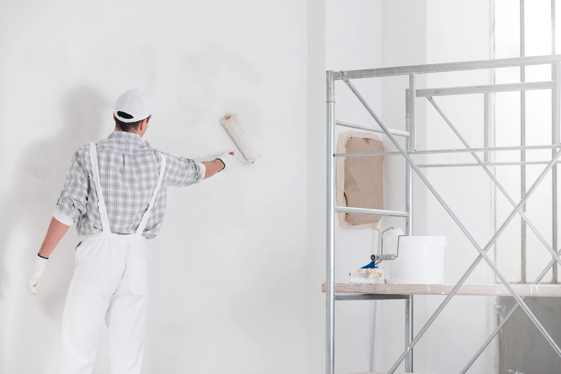 Un peintre en bâtiment applique de la peinture blanche sur un mur intérieur à l'aide d'un rouleau à peinture