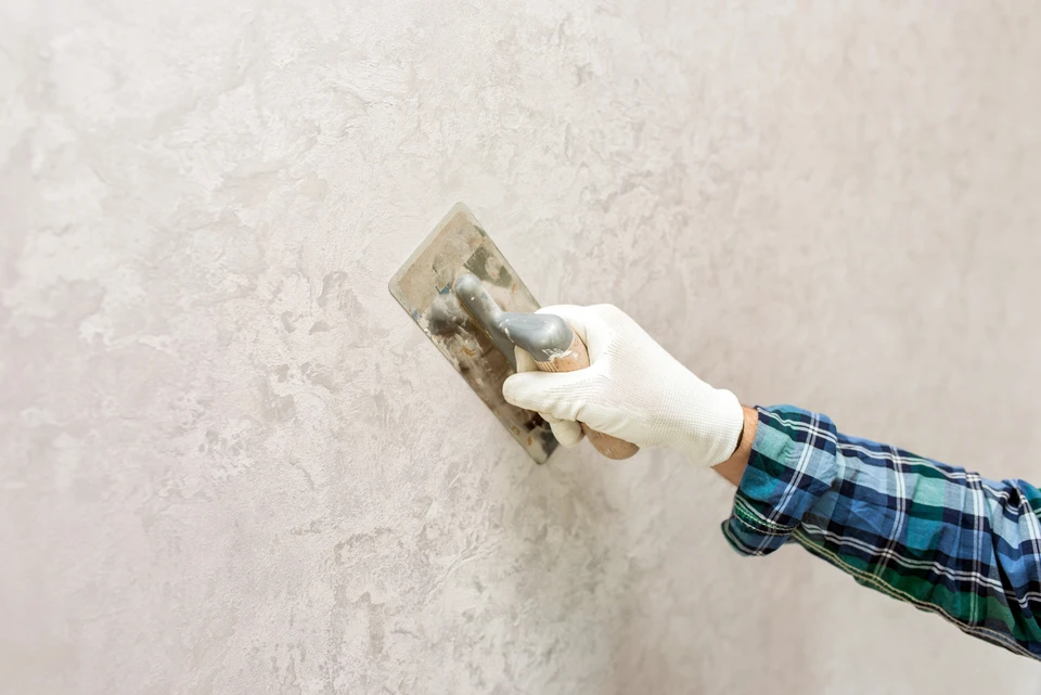Ouvrier en tenue de travail applique un enduit sur un mur intérieur à l'aide d'une taloche
