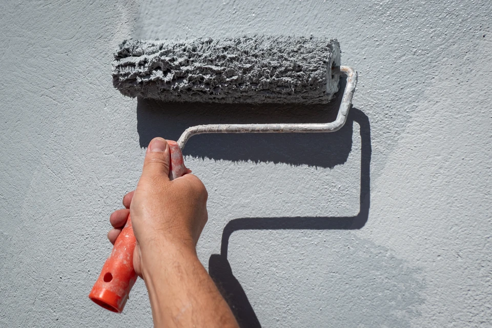 Un peintre en bâtiment applique de la peinture blanche sur un mur intérieur à l'aide d'un rouleau à peinture