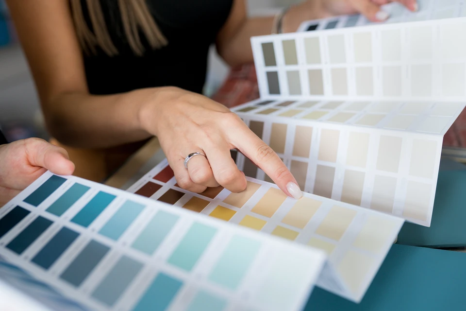 Professionnel en chemise travaillant sur ordinateur dans bureau lumineux, consultant nuancier de couleurs et palette chromatique étalés sur table en bois